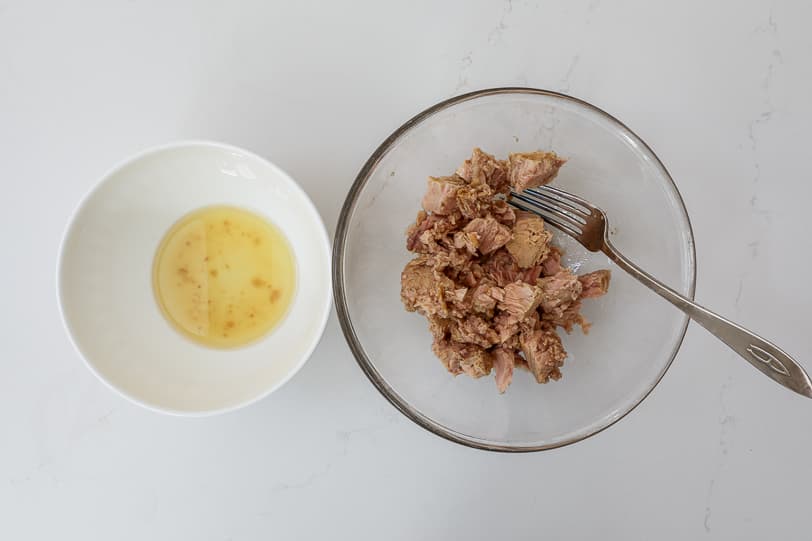 An image of olive oil from a can of tuna in a bowl and flaked tuna in another bowl.