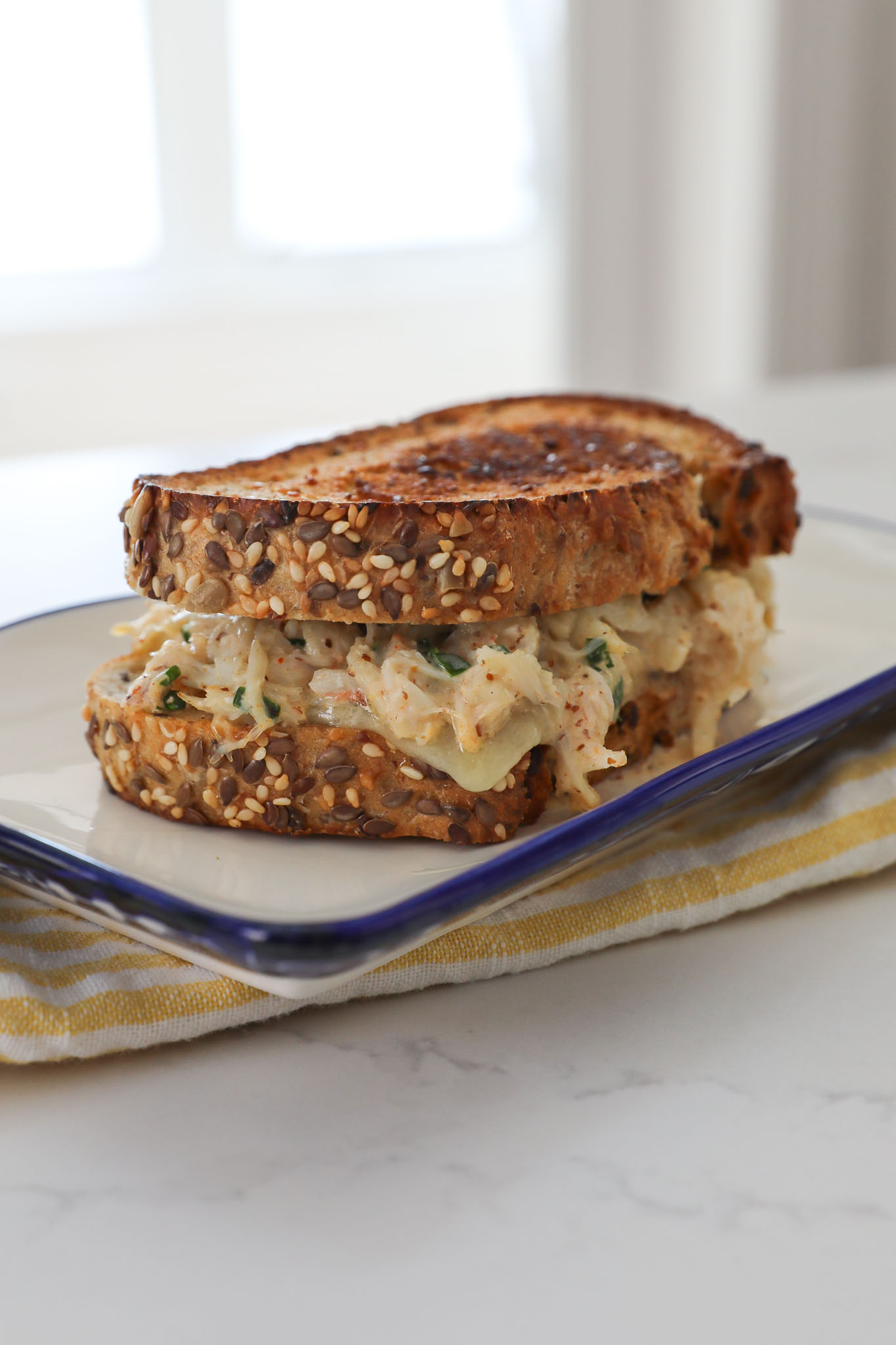A side view image of a crab grilled cheese on a white rectangular plate. 