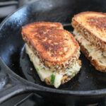 An image of 2 crab grilled cheeses in a cast-iron skillet.