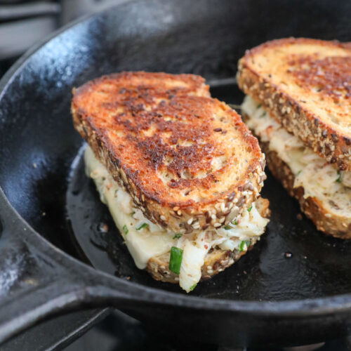 An image of 2 crab grilled cheeses in a cast-iron skillet.