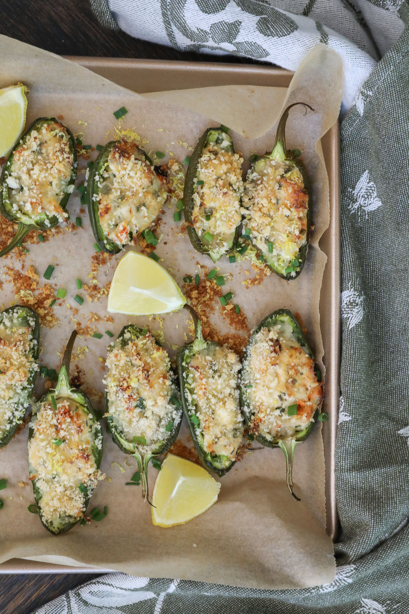 An overhead image of crab jalapeno poppers on a baking sheet with lemon wedges. 
