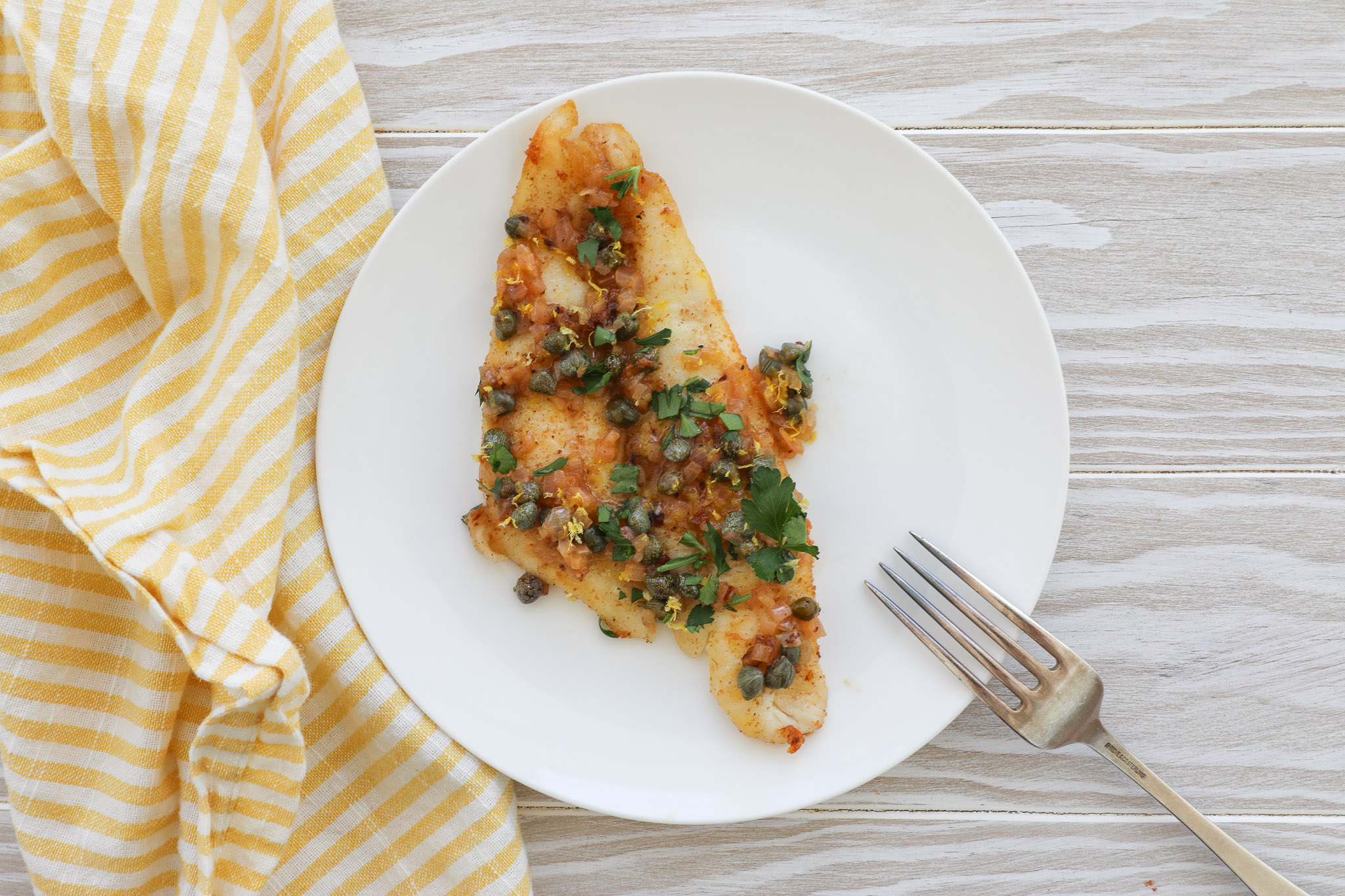 An image of a sole piccata filet on a small white plater. 